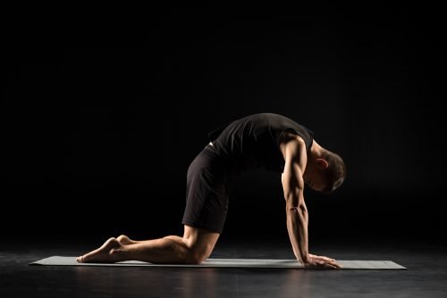 Man performing Cat–Cow stretch, illustrating yoga’s role in recovery and injury prevention through improved circulation, reduced tension, and nervous system regulation.