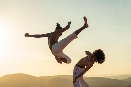 Capoeirista executing a spinning aerial kick as an opponent evades during a live exchange.