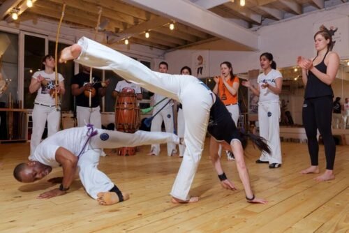 Two Capoeira practitioners facing one another and reading movement, distance, and positioning during a Capoeira game.