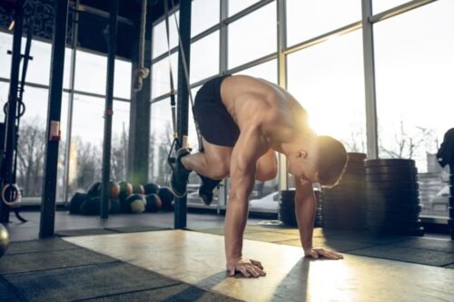 Man performing TRX suspension training exercises in a gym, demonstrating strength, stability, movement quality, and functional fitness.