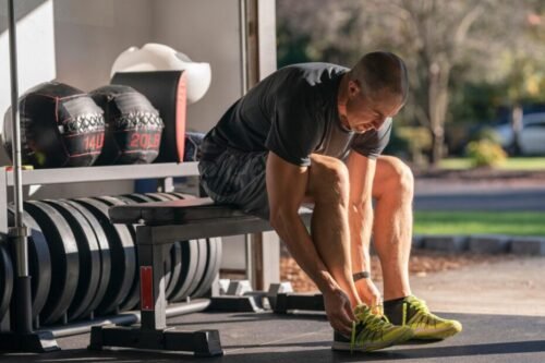 Man sitting in a garage gym tying his training shoes before a workout, representing routine, discipline, and making training part of daily life.