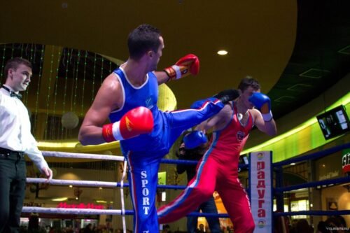 Two Savate competitors sparring in a boxing ring under the supervision of a referee during a modern Savate competition.
