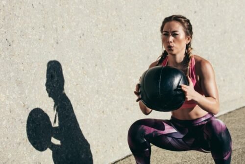 Woman squatting outdoors with a medicine ball, symbolising home training for Hyrox without full gym access.