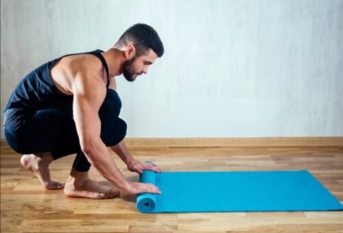 Man rolling out a yoga mat, symbolising the first steps of a beginner starting their yoga practice and learning foundational basics.