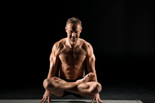 Man in a seated lift pose, supporting his body with fingertips — representing yoga’s fusion of strength, control, and mastery developed through disciplined practice.