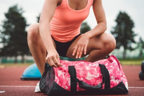 Young woman on running track unzipping gym bag preparing to train showing structured routine and readiness