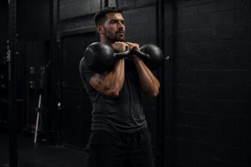 Athlete holding two kettlebells in a strong front rack position demonstrating full-body tension and hardstyle kettlebell technique.
