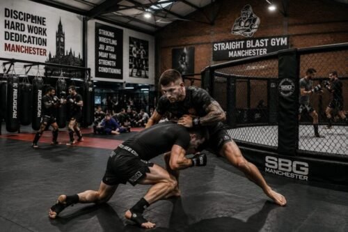 Mixed martial artists sparring inside a modern gym in Manchester, combining striking, wrestling, and grappling skills.