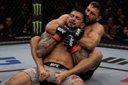 Two MMA fighters grappling on the ground as one controls the other's back while the defending fighter fights the hands and looks to escape.