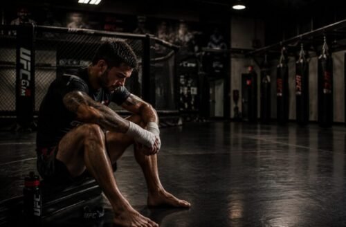 Tired MMA fighter sitting after training with his gloves removed and hand wraps still on.