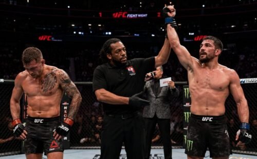 MMA fighter having his hand raised after a fight as his opponent looks down following the result.