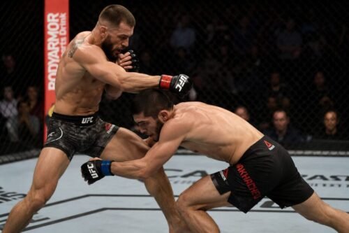 MMA fighter drops beneath a punch combination to attack a double-leg takedown inside the cage.