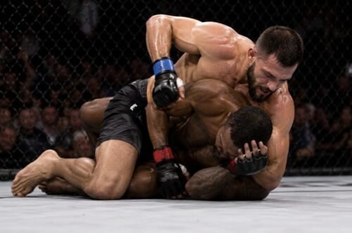 MMA fighter controls an opponent from side control while preparing to strike as the defender frames and tries to escape.