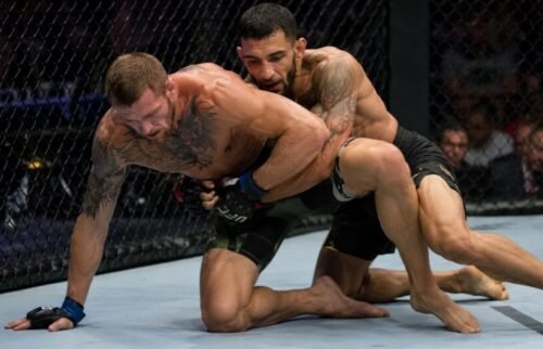 One MMA fighter works back to their feet while the opponent circles behind and secures control around the waist.
