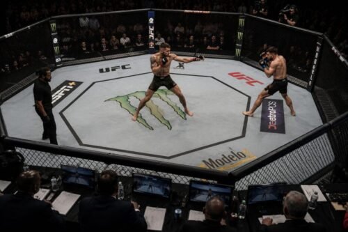Elevated view of an MMA fighter controlling the centre while forcing an opponent towards the edge of the cage.