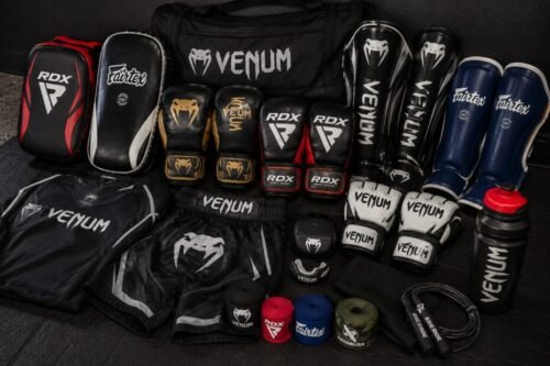 MMA kit arranged together, including boxing gloves, MMA gloves, shin guards, pads, wraps, mouthguard, clothing and a gym bag.
