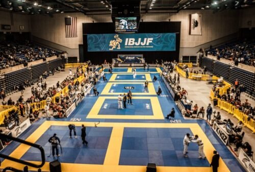 Panoramic view of a major Brazilian Jiu-Jitsu tournament with multiple competition mats, referees, competitors, coaches, and spectators inside a large indoor arena.